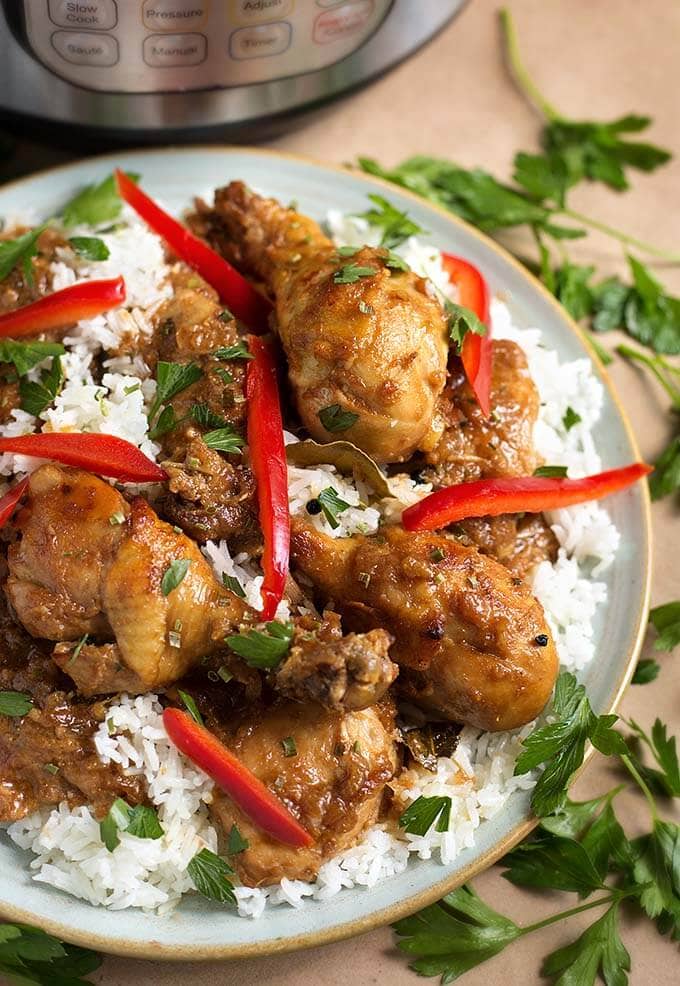 Chicken Adobo Filipino with rice on a white plate garnished with red peppers, cilantro