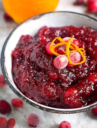 Cranberry Sauce in a white bowl with black rim surrounded by frosted cranberries