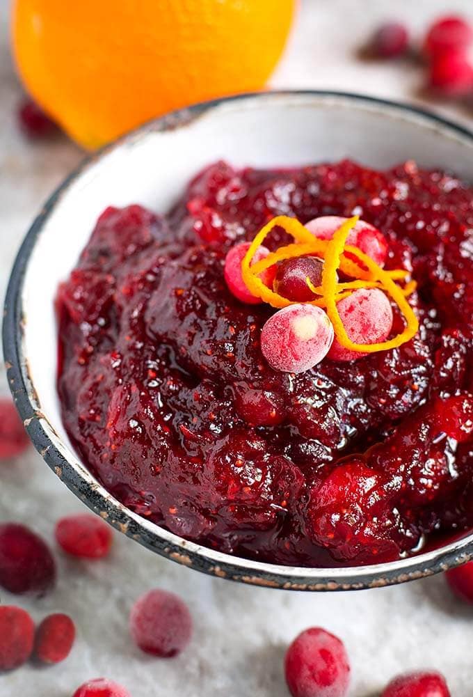 Cranberry Sauce in a white bowl with a black rim topped with frosted cranberries and orange zest