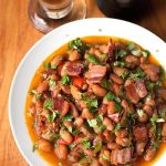 Drunken Beans (Frijoles Borrachos), in a white bowl next to glass of beer on a wooden board