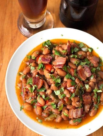 Drunken Beans (Frijoles Borrachos), in a white bowl next to glass of beer on a wooden board