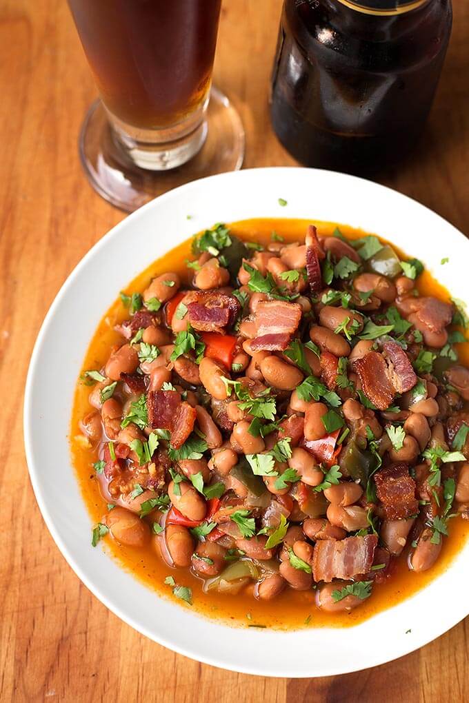 Drunken Beans (Frijoles Borrachos), in a white bowl next to glass of beer on a wooden board