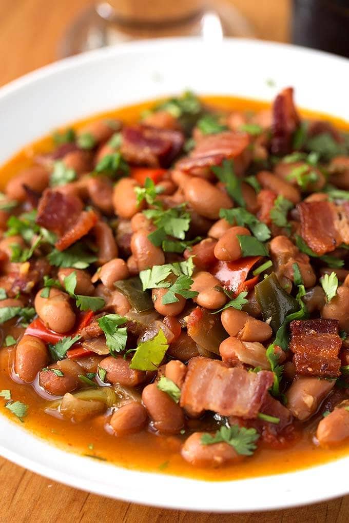 Close up of Drunken Beans, Frijoles Borrachos, in a white bowl on wooden board