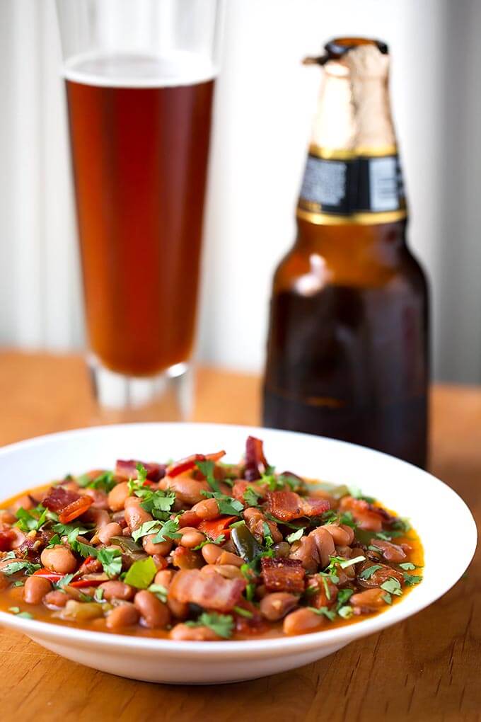 Drunken Beans (Frijoles Borrachos), in a white bowl next to glass of beer on a wooden board