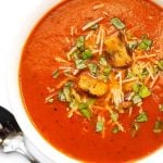 Tomato Soup in a white bowl next to silver spoon on a white background