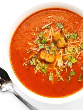 Tomato Soup in a white bowl next to silver spoon on a white background