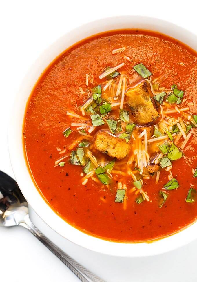  Tomato Soup in a white bowl next to silver spoon on a white background