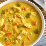 Mulligatawny Soup in a white bowl next to spoon on bamboo mat