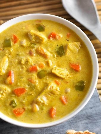 Mulligatawny Soup in a white bowl next to spoon on bamboo mat