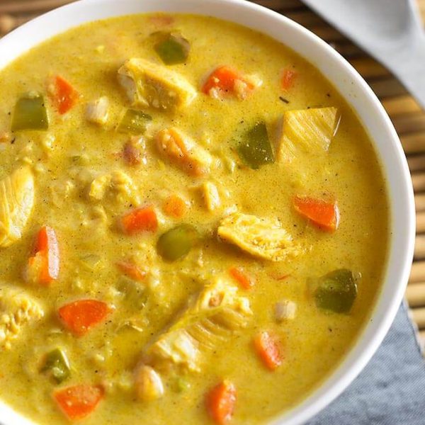Mulligatawny Soup in a white bowl next to spoon on bamboo mat
