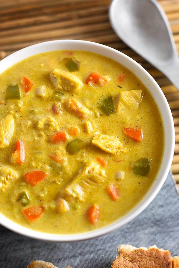 Mulligatawny Soup in a white bowl next to spoon on bamboo mat