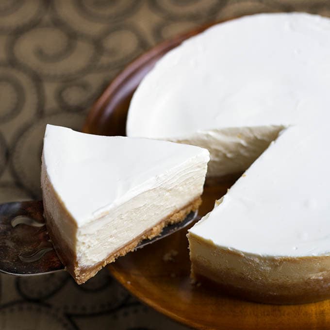 Plain slice of New York Cheesecake being lifted from rest of cake on brown plate