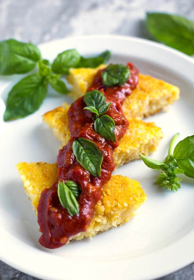 Polenta slices on a white plate with red sauce and basil leaves