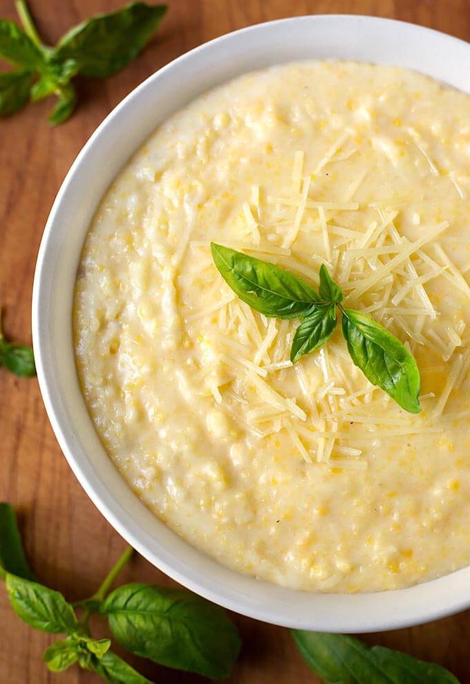 Polenta in a white bowl on a wooden board garnished with basil