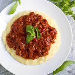 Chorizo Tomato Sauce topping polenta on a white plate garnished with basil