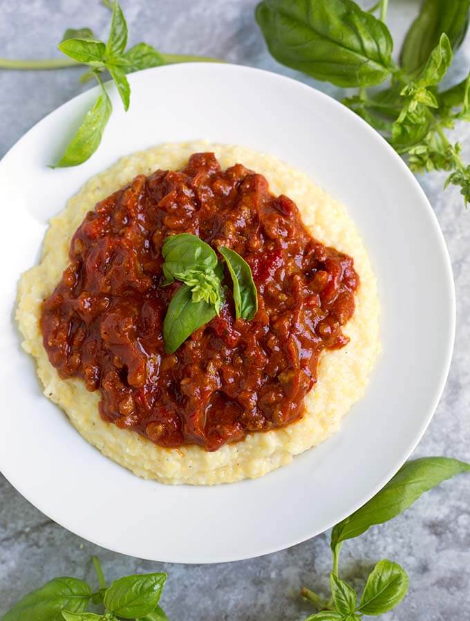 Chorizo Tomato Sauce topping polenta on a white plate garnished with basil