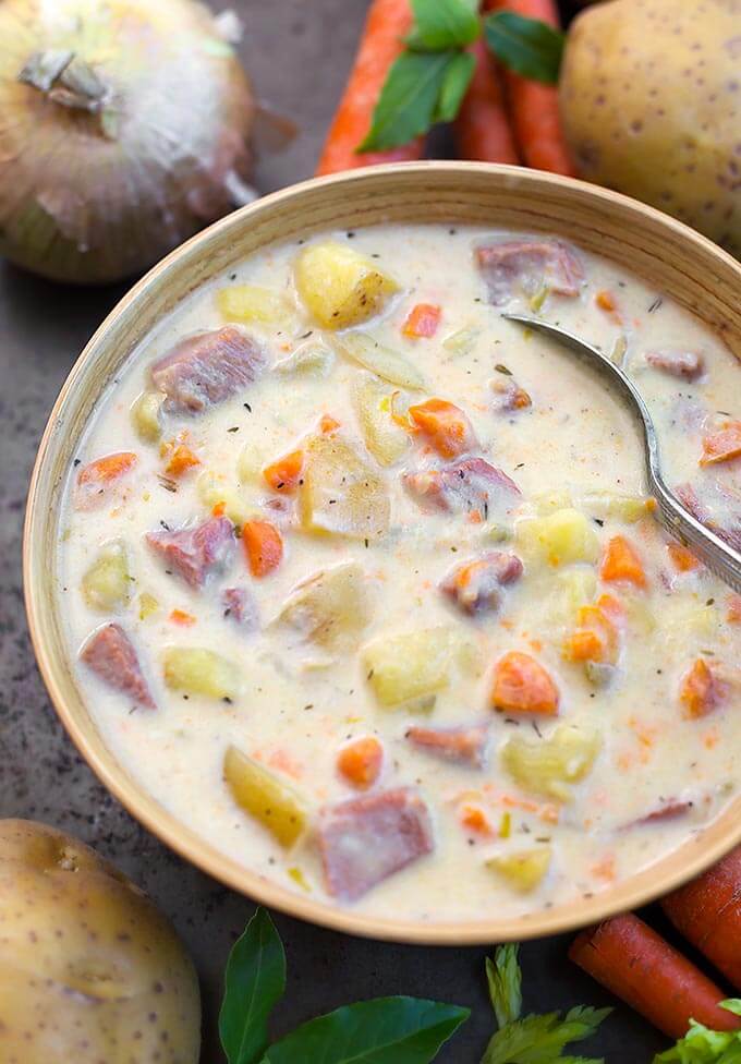 Instant Pot Potato Ham Soup in beige bowl with spoon surrounded by vegetables