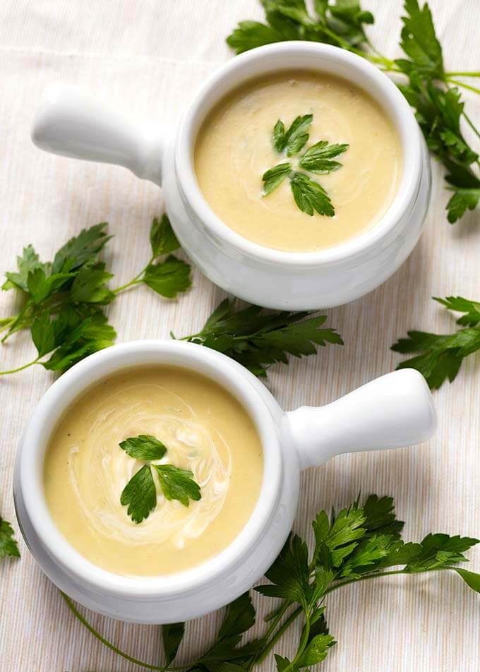 Two white bowls with handles with Potato Leek Soup garnished with parsley 