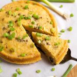 Cut Slice of Southwest Corn Pudding garnished with green onion being lifted from rest of pudding