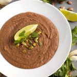 Refried Beans in a white bowl topped with papitas cilantro and lime