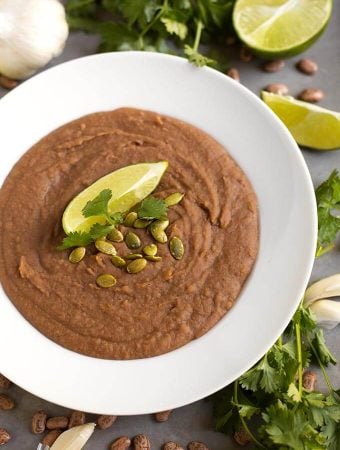 Refried Beans in a white bowl topped with papitas cilantro and lime