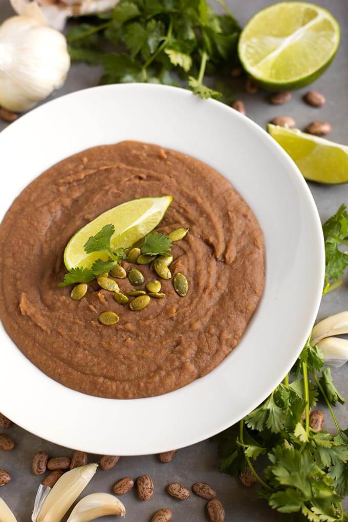 Refried Beans in a white bowl topped with papitas cilantro and lime