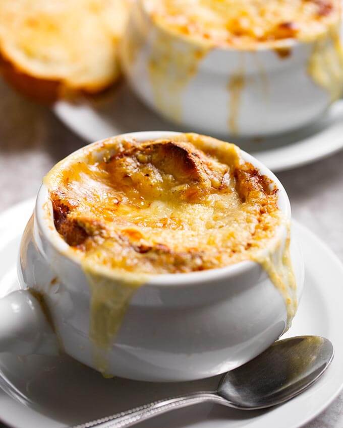 Picture of french onion soup in a small handled white bowl with a silver spoon