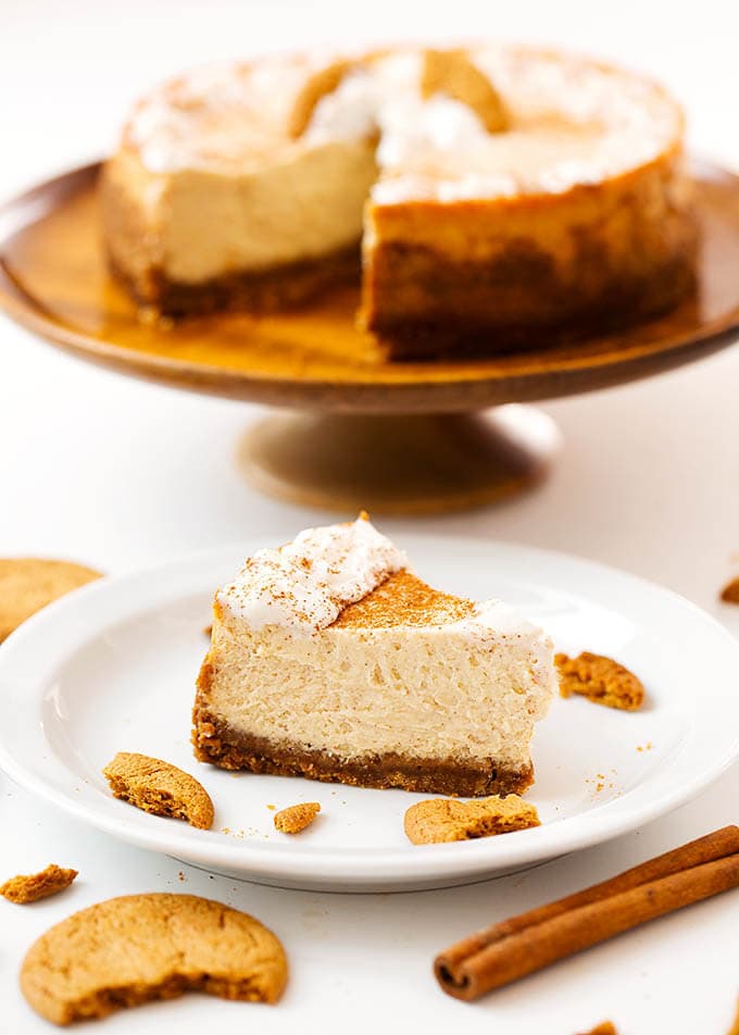 Slice of Eggnog Cheesecake on a white plate in front of cheesecake on brown cake stand