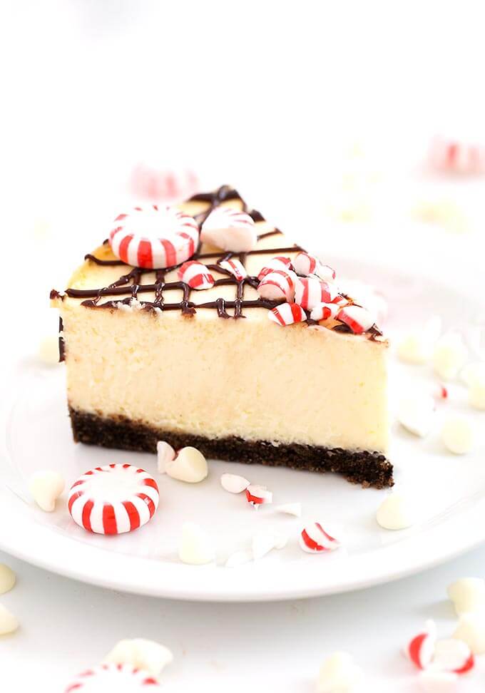 Slice of  White Chocolate Peppermint Cheesecake on white plate garnished with broken peppermint candies