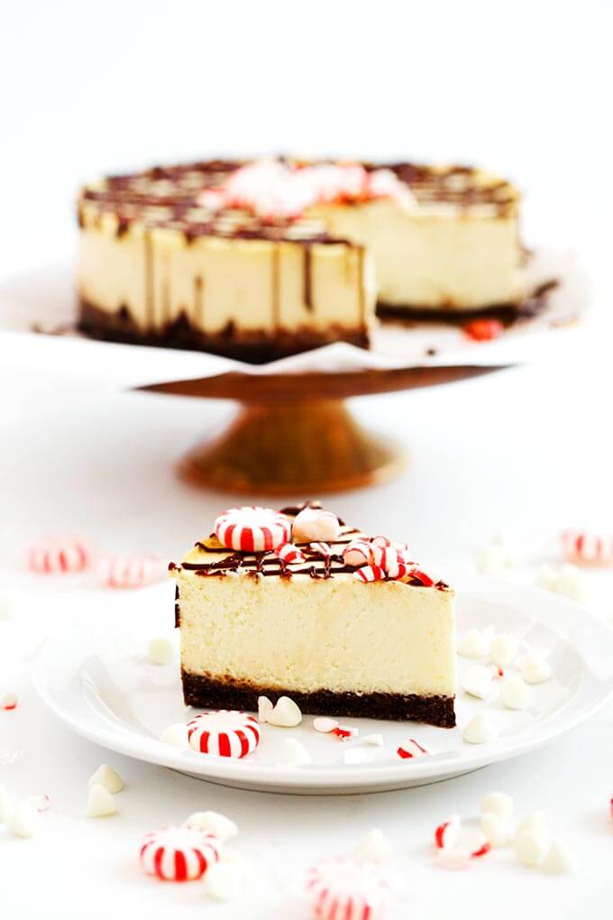 Slice of White Chocolate Peppermint on a white plate in front of rest of cheesecake on a cake stand 