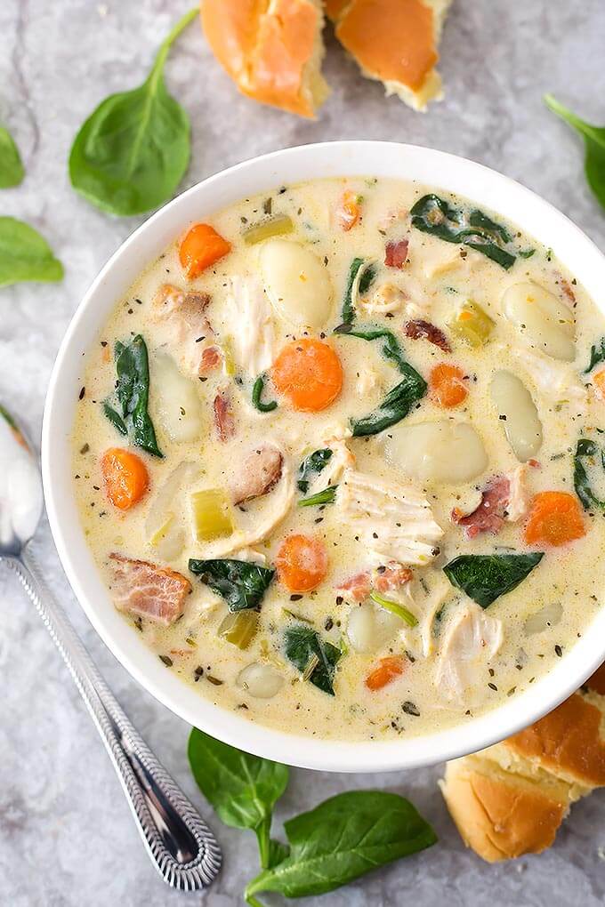 Creamy Chicken Gnocchi Soup in a white bowl next to a silver spoon on marble background