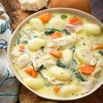 Creamy Chicken Gnocchi Soup on a wooden board with two rolls next to two golden spoons