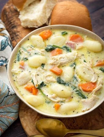 Creamy Chicken Gnocchi Soup on a wooden board with two rolls next to two golden spoons