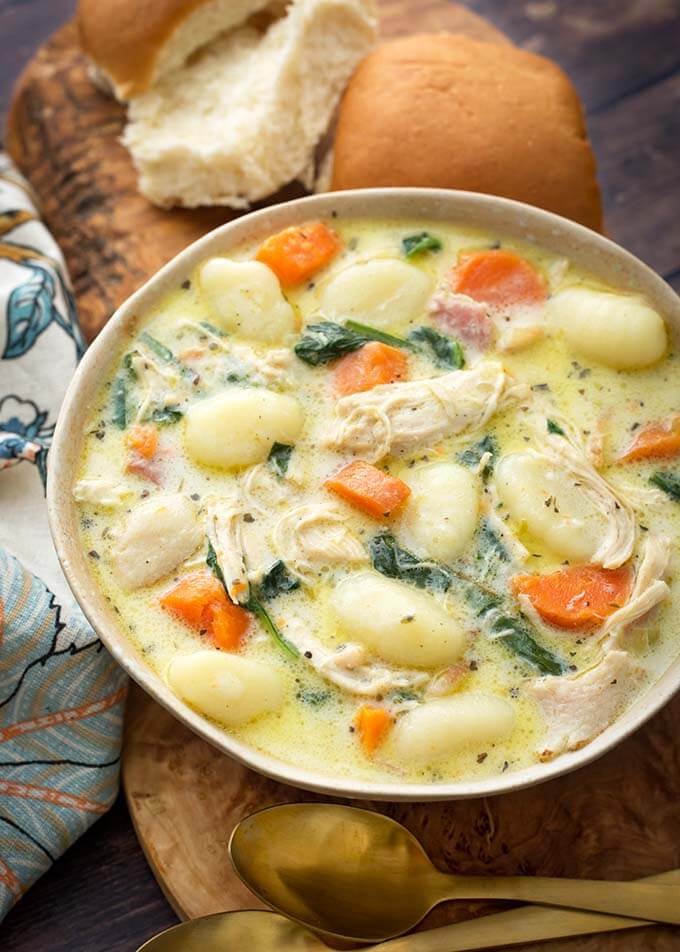 Creamy Chicken Gnocchi Soup on a wooden board with two rolls next to two golden spoons