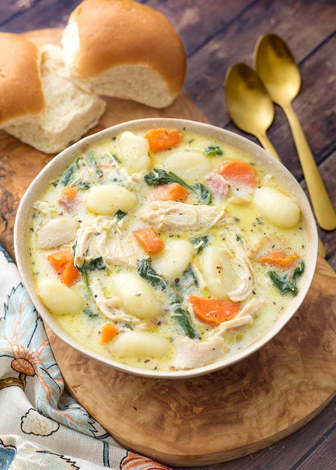 Creamy Chicken Gnocchi Soup on a wooden board with two rolls next to two golden spoons