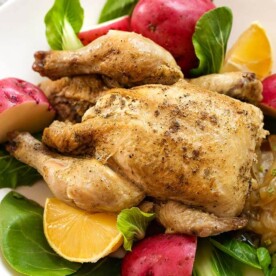 Cornish Game Hen on a white plate with potatoes and vegetables