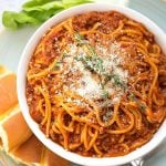 Spaghetti in a white bowl on plate with bread fork and green vegetable