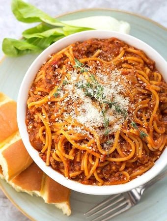 Spaghetti in a white bowl on plate with bread fork and green vegetable