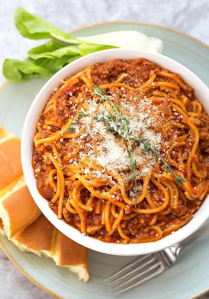 Spaghetti in a white bowl on plate with bread fork and green vegetable