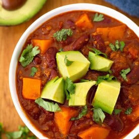 Sweet potato chili in a white bowl on wooden board garnished with chopped avocados