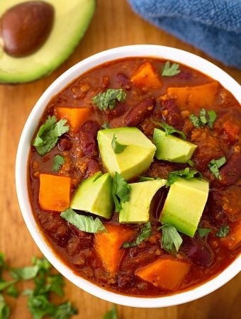 Sweet potato chili in a white bowl on wooden board garnished with chopped avocados