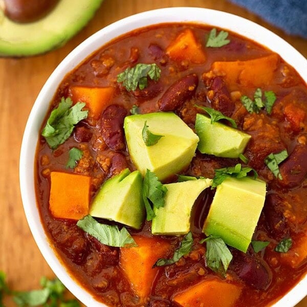 Sweet potato chili in a white bowl on wooden board garnished with chopped avocados