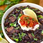 Black Beans in a white bowl on a wooden board garnished with lime wedge and cilantro