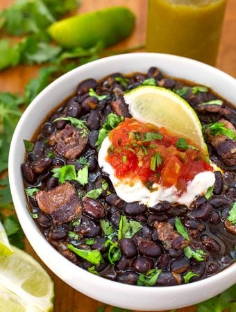 Black Beans in a white bowl on a wooden board garnished with lime wedge and cilantro