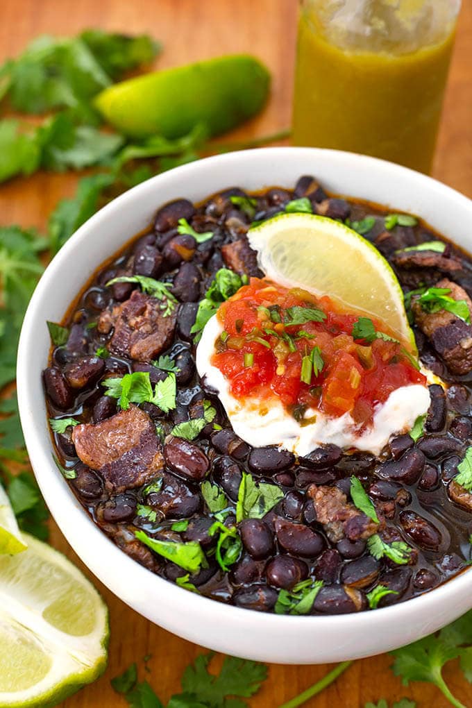 Black Beans in a white bowl on a wooden board garnished with lime wedge and cilantro