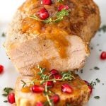 Balsamic Apple Pork Tenderloin garnished with pomegranate and thyme on a white plate