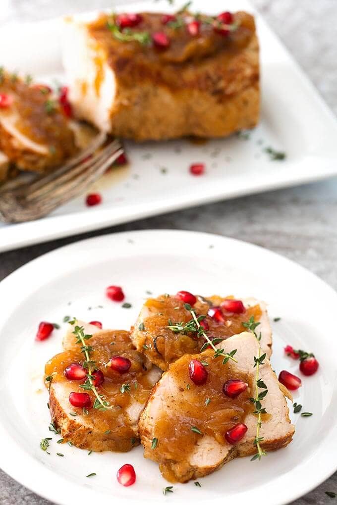 Sliced Balsamic Apple Pork Tenderloin garnished with pomegranate and thyme on a white plate