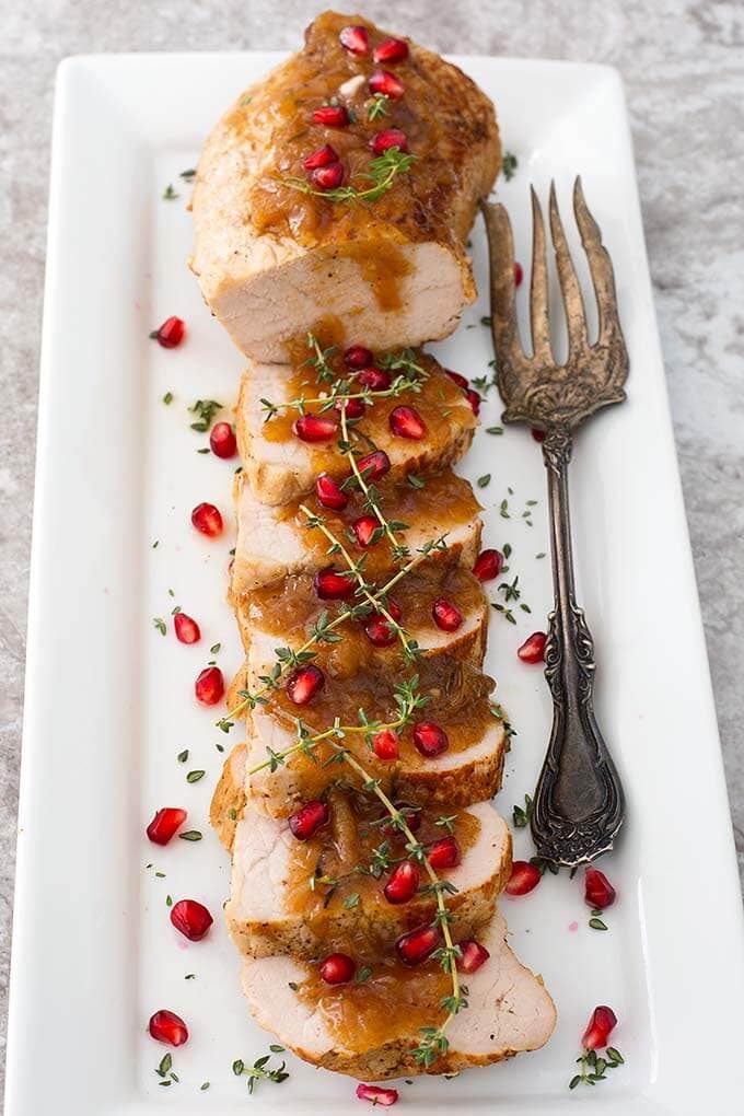 Sliced Balsamic Apple Pork Tenderloin Balsamic Apple Pork Tenderloin garnished with pomegranate and thyme on a white plate