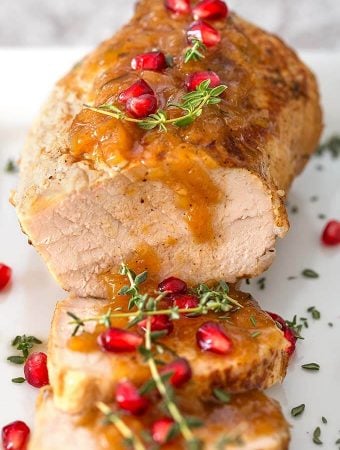 Balsamic Apple Pork Tenderloin garnished with pomegranate and thyme on a white plate