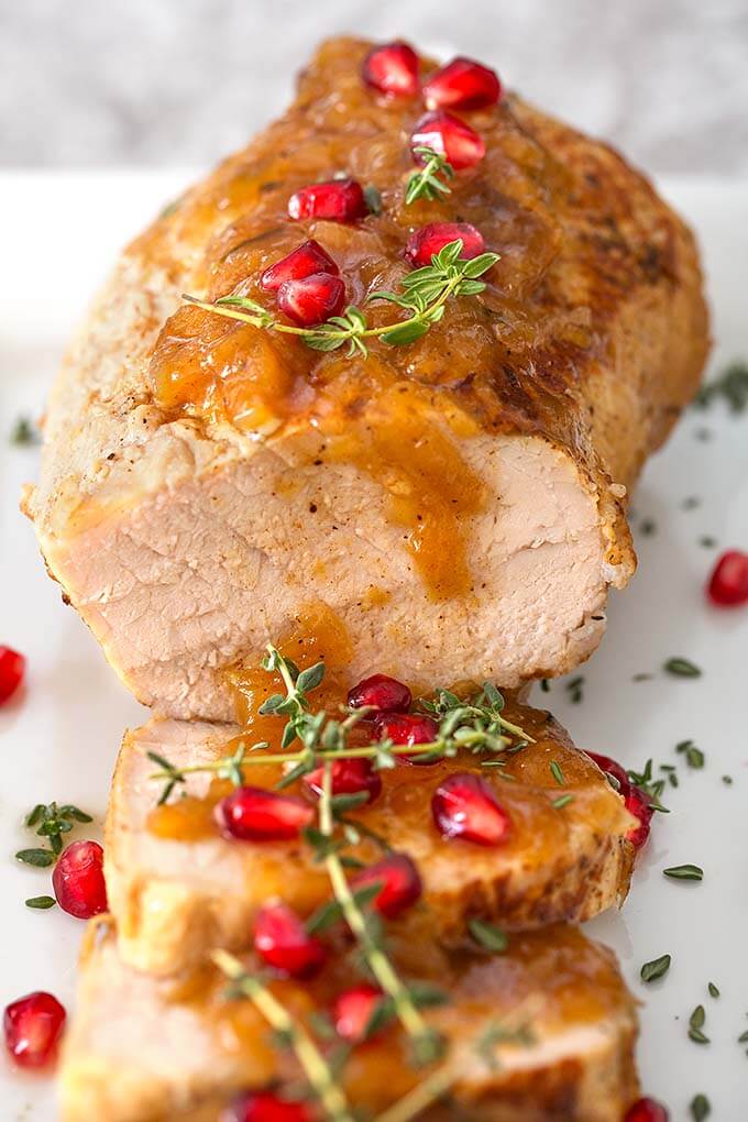 Balsamic Apple Pork Tenderloin garnished with pomegranate and thyme on a white plate